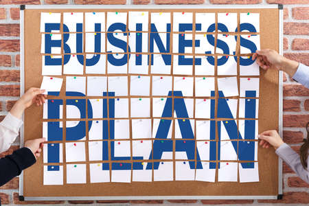 Business People Hands Holding Paper Notes On Corkboard With Business Plan Text Written On Itの写真素材