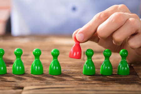 Close-up Of A Person Placing Red Figures In The Green Row Over The Wooden Deskの写真素材