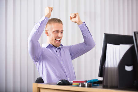 Successful Young Businessman Raising His Hands In Office