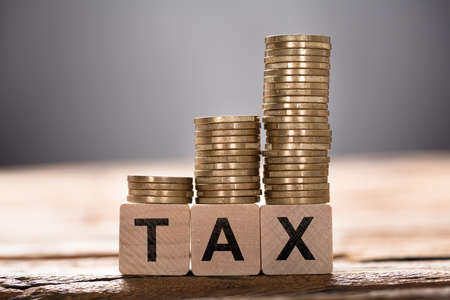 Closeup of tax text written on wooden blocks with stacked coins