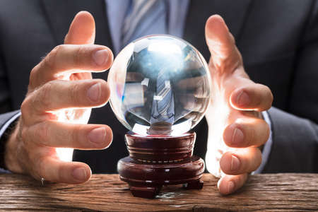 Midsection of businessman covering crystal ball at wooden tableの写真素材