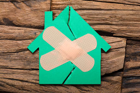 Closeup of broken house with crossed band aid on woodの写真素材