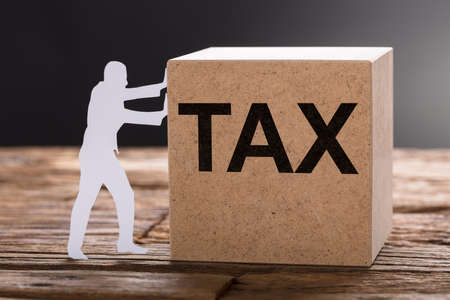 Closeup of paper man pushing tax wooden block on table against gray backgroundの写真素材