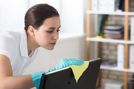 A Young Woman Cleaning The Desktop With Yellow Rag In Officeの写真素材