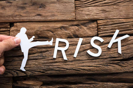 Closeup of hand holding paper businessman kicking word risk on woodの写真素材