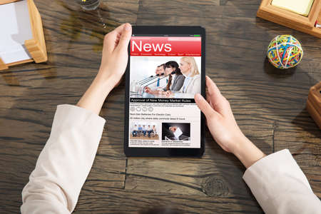 Woman Holding Digital Tablet With A Screen Showing Unfolds Scandal News Over The Wooden Deskの写真素材