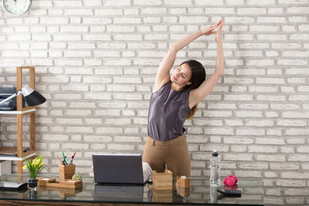 Young Businesswoman Stretching At Workplace In Officeの写真素材