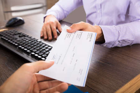 Close-up Of A Businessman Giving Cheque To Her Colleague At Workplace In Office