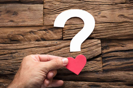 Closeup of hand holding question mark with heart on wood