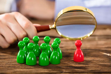 Close-up Of A Human Hand Examining Red Plastic Figure With Magnifying Glass Over Wooden Deskの写真素材