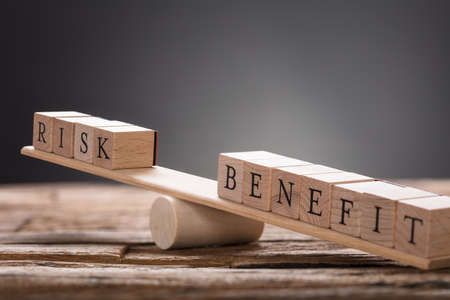 Closeup of risk and benefit wooden blocks on seesaw