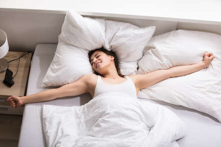 Elevated View Of A Young Woman Stretching Her Hands On Bed