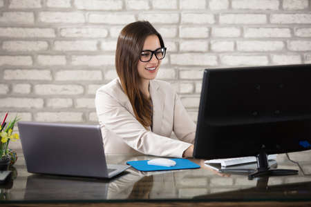 Young Smiling Young Businesswoman With Eyeglasses Using Computer In Office