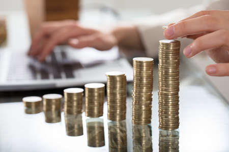 A Businessperson Hand Put Coins To Stack Of Coins On Glass Desk At Workplace