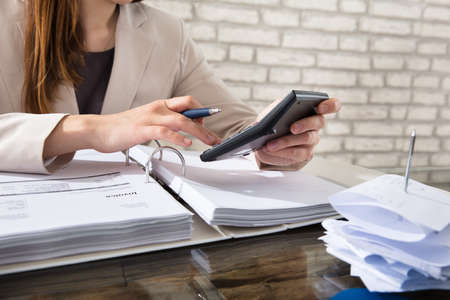 Close-up Of A Businesswoman Calculating Invoice Using Calculator At Workplaceの写真素材