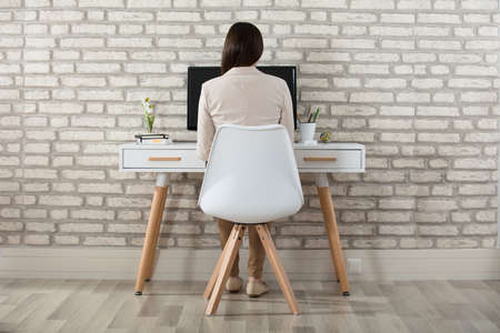 Rear View Of A Businesswoman Sitting In Front Of Computer At Workplaceの写真素材
