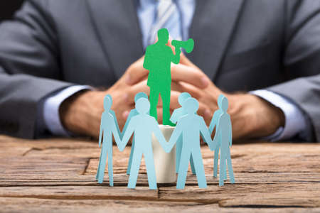 Green paper executive speaking through megaphone surrounded by team on wooden tableの写真素材