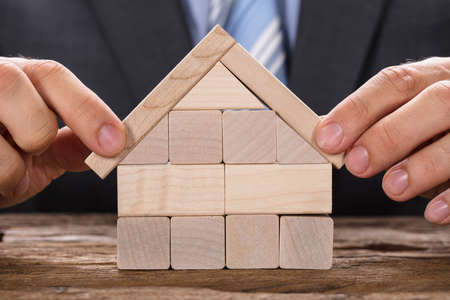 Midsection of businessman making model house with wooden blocks at tableの写真素材