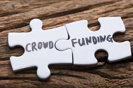 Closeup of connected crowd funding jigsaw pieces on woodの写真素材