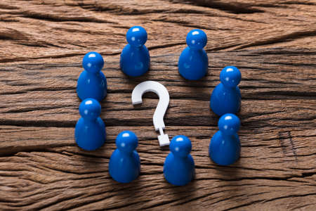 Closeup of question mark surrounded by blue pawn figurines on woodの写真素材