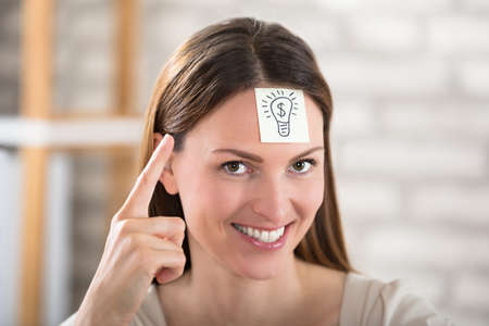 Close-up Of A Businesswoman With Electric Bulb Drawn Over Sticky Note On His Foreheadの写真素材