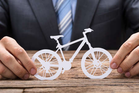 Midsection of businessman holding paper bicycle at wooden table