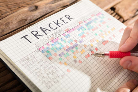 Close-up Of A Person's Hand Drawing Tracker Chart On Grid Notebookの写真素材