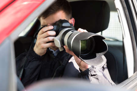Side View Of A Private Detective Sitting Inside Car Photographing With Slr Camera