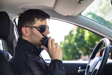 Close-up Of A Male Private Detective Sitting Inside Car Talking On Walkie Talkie