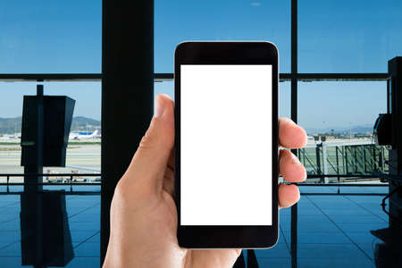 Closeup of hand holding mobile phone with white screen in airportの写真素材