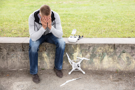 Young Worried Man With Broken Drone Sitting In The Parkのeditorial素材