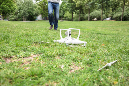 White Quadrocopter Fallen On Grass With Operator Running In The Backgroundのeditorial素材