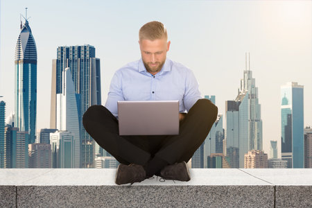 Young Businessman Sitting On The Rooftop Of A Skyscraper Using Laptopのeditorial素材