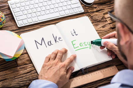 Businessman Writing Make It Easy Text On Notebook With Green Marker Over The Office Deskの写真素材