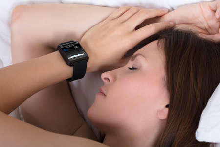 Close-up Of A Woman Sleeping With Smart Watch Showing Heartbeat Rate On Bedの写真素材
