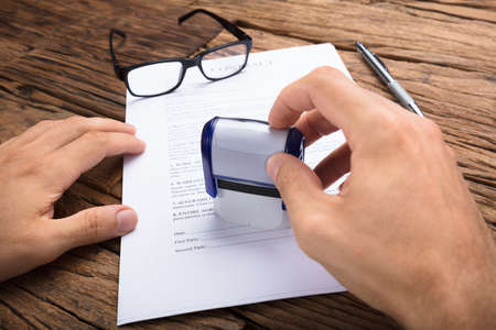 Cropped hands of businessman stamping contract paper at wooden tableの写真素材