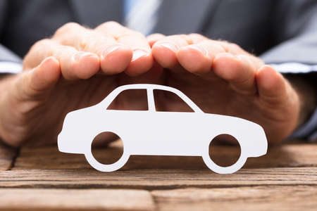 Cropped image of businessman covering paper car on wooden tableの写真素材