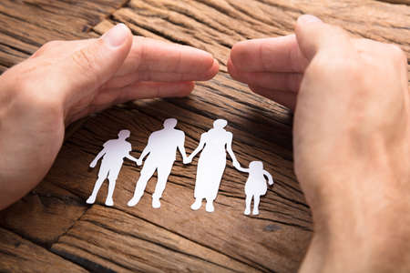 Cropped image of businessman covering paper family at wooden tableの写真素材