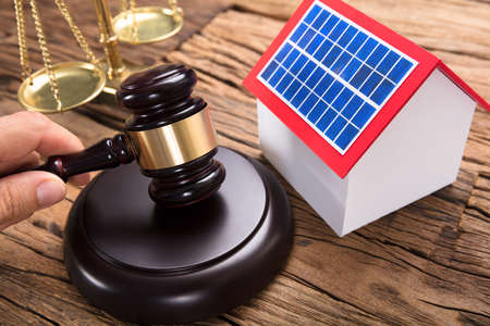 Judge hitting mallet by solar model home and justice scale on wooden table in courtroom