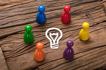 High angle view of multicolored pawn figurines surrounding paper light bulb on wooden tableの写真素材