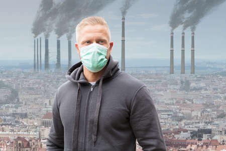 Close-up Of A Man Wearing Mouth Mask Against Smoke Emitting From Factory Chimneysの写真素材