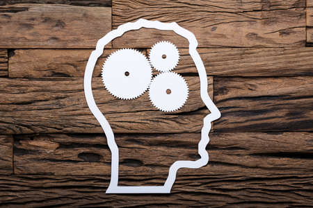 Directly above shot of paper businessman's head outline with metallic gears on wooden tableの写真素材