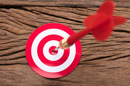 Closeup of red arrow in dartboard on wooden table