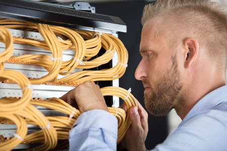 Close-up Of Young Male Technician Checking Server's Wires In Data Centerの写真素材