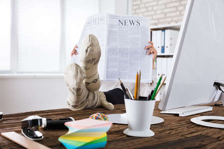 Businessperson Wearing Socks Reading Newspaper In Officeの写真素材