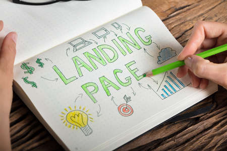 Close-up Of A Human Hand Drawing Landing Page Concept On Notebook At Desk