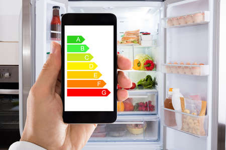 Closeup of man's hand using energy label on mobile phone against refrigerator at homeの写真素材
