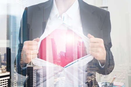 Double exposure of businesswoman tearing shirt over city backgroundの写真素材