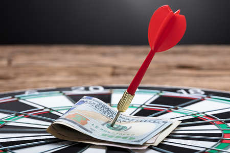 Closeup of arrow in papernotes on dartboard at table against black backgroundの写真素材