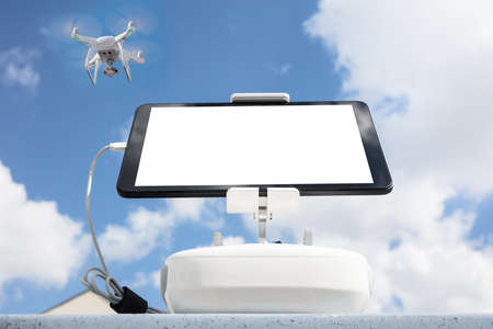 Low angle view of digital tablet attached to controller while drone flying in skyの写真素材